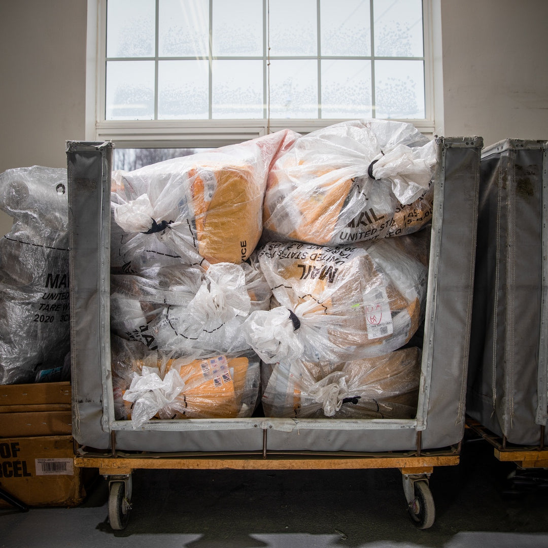 A rolling cart filled to the brim with packages from the post office for Darn Tough