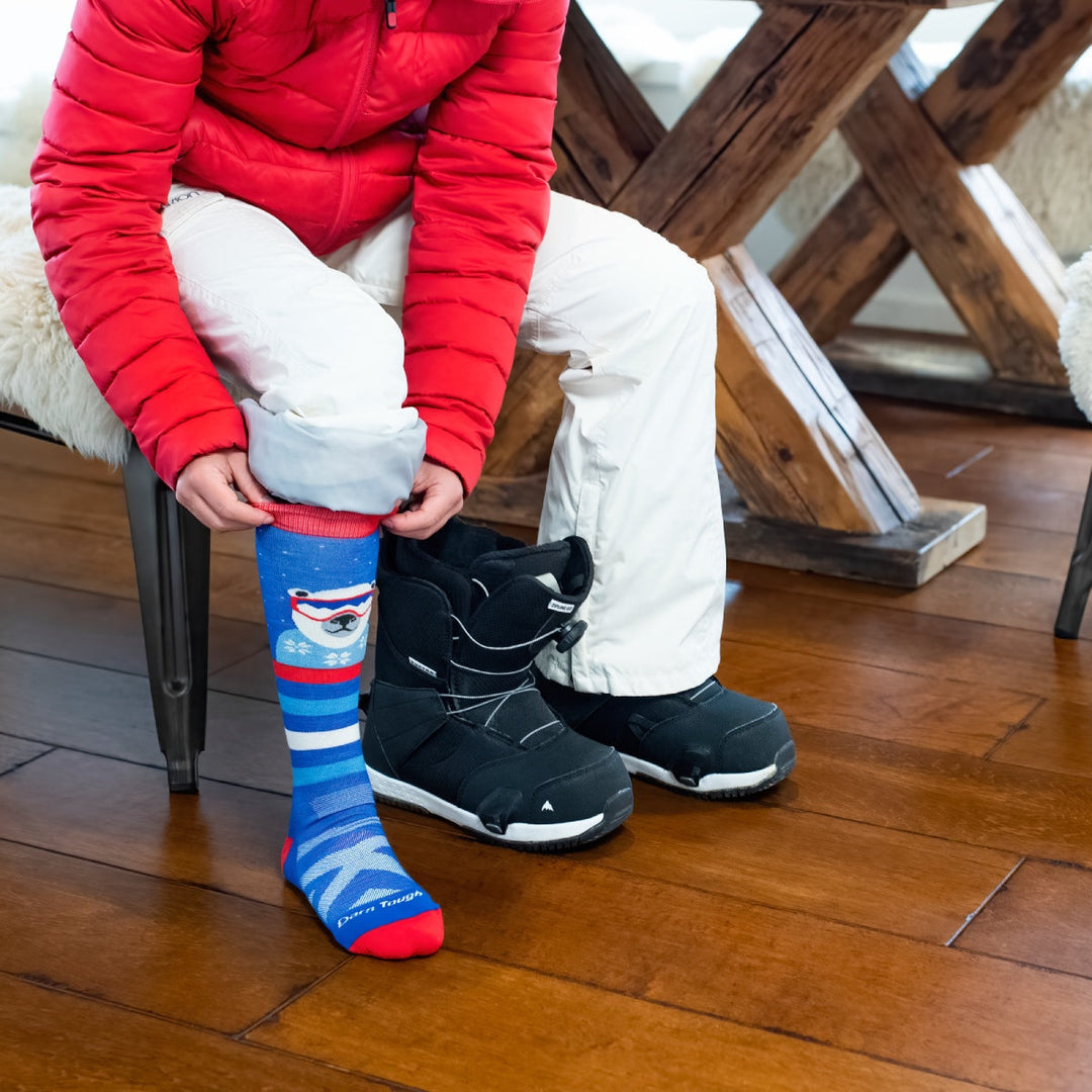 Person in snow gear pulling on warm socks with polar bears on them