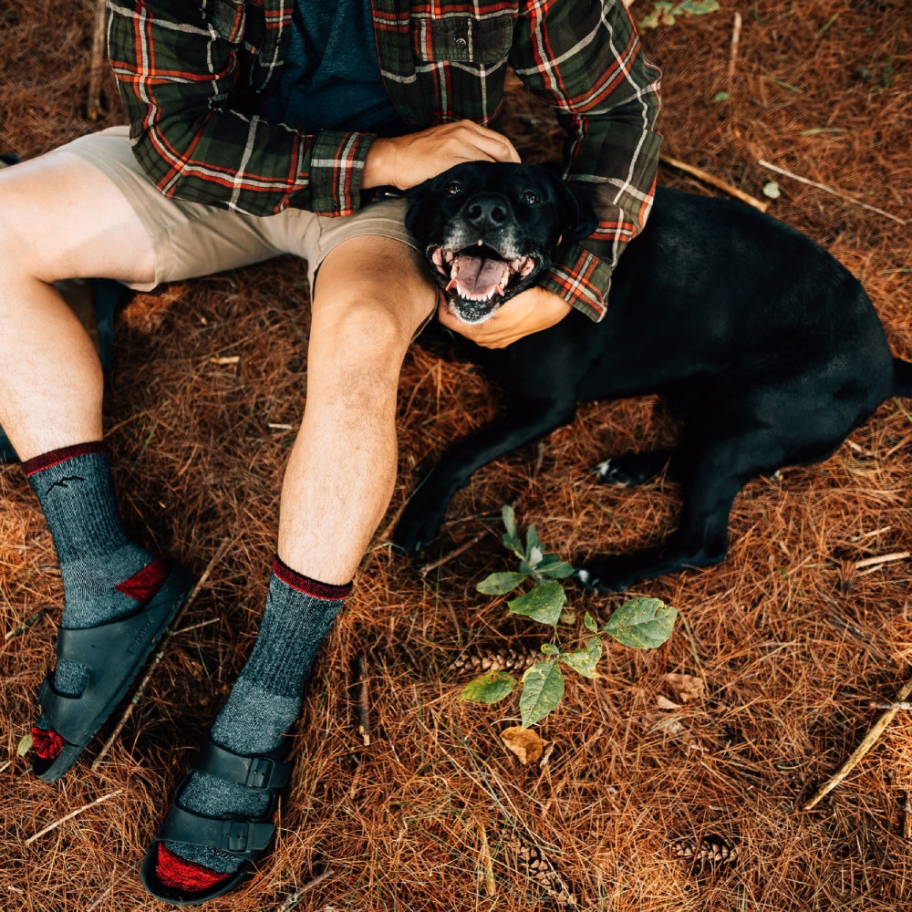 A hiker seated on ground petting dog, as dog smiles for camera