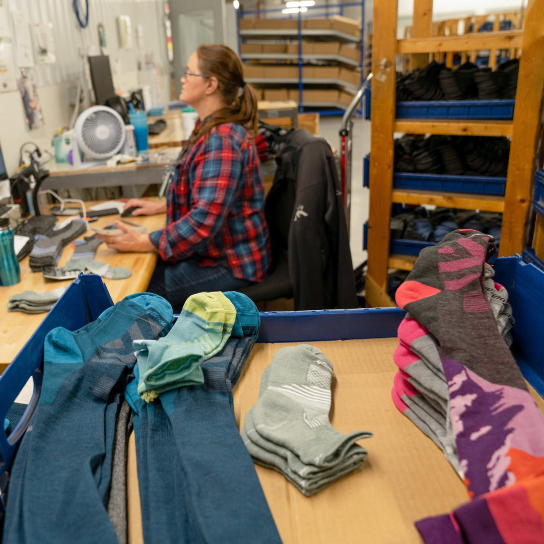 Darn Tough employee sitting at desk, an array of socks nearby, all guaranteed for life