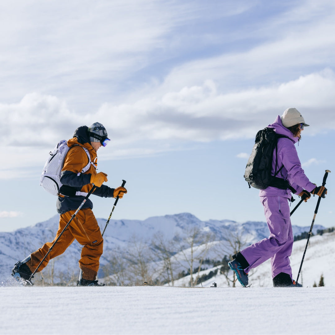 Two people on a mountain wearing backpacks and equipment for backcountry skiing
