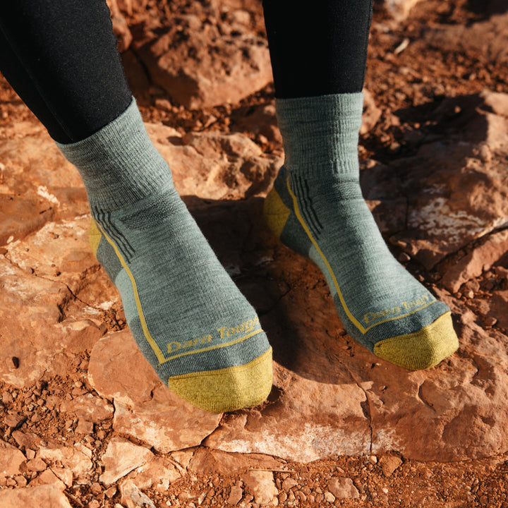 Model wearing 1958 socks in Sage colorway without shoes on red desert rocks
