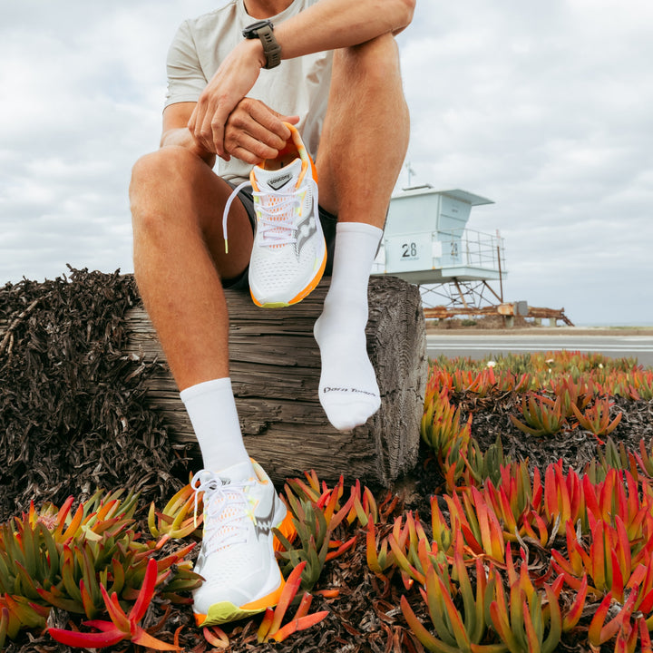 model sitting on log holding one shoe wearing the 1035 micro crew running sock in white colorway