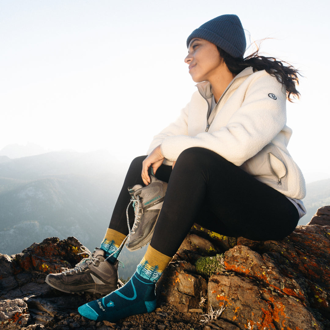 Full model image, sitting on Rock ledge putting on shoes with 5013 Dark teal in view