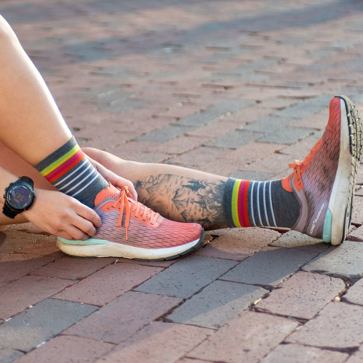 Woman sits on brick pavement wearing running shoes and Women's Stride Micro Crew Ultra-Lightweight Running Sock in Gray