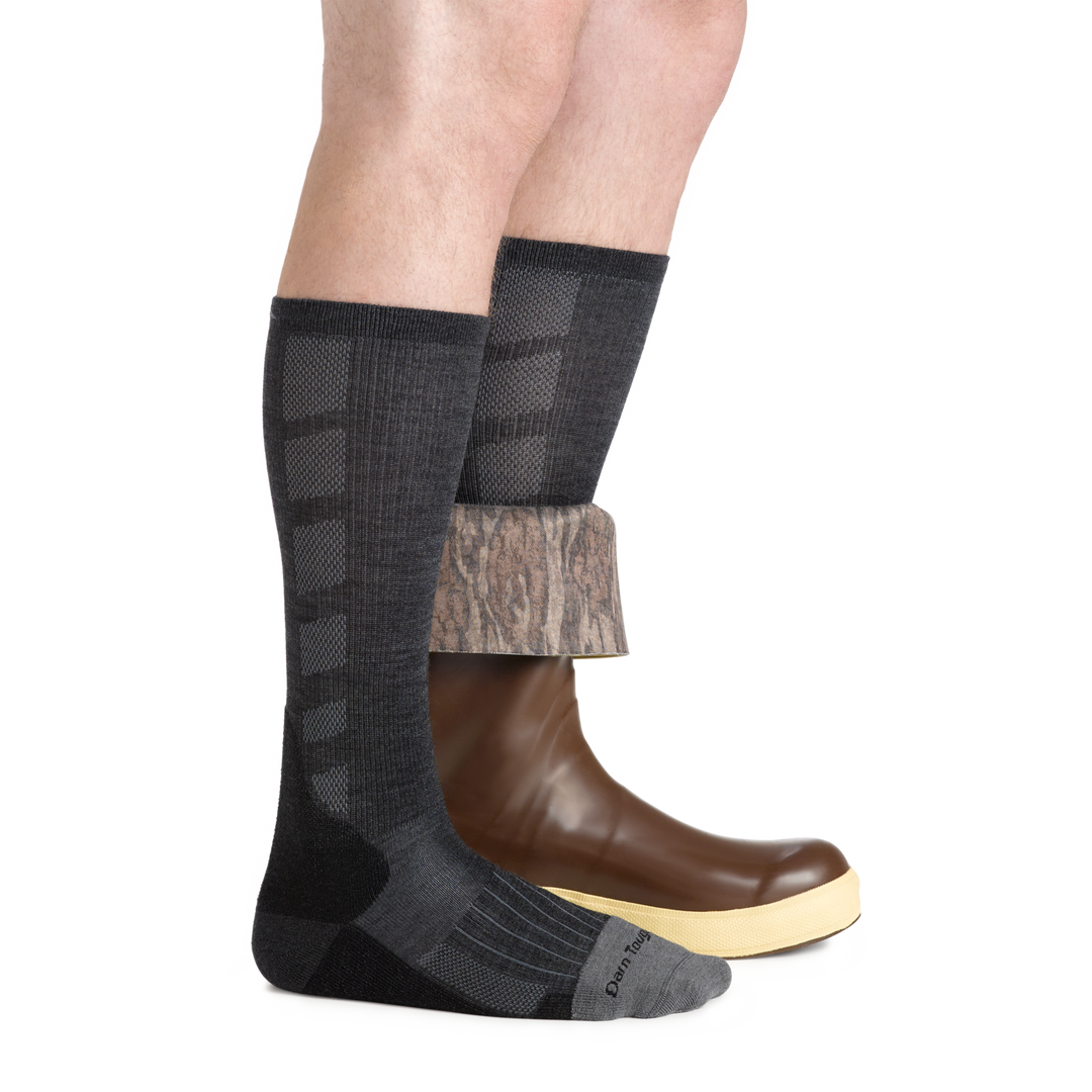 Side studio shot of model wearing men's stanley k mid-calf work sock in gravel gray with rubber boot on left foot folded half down