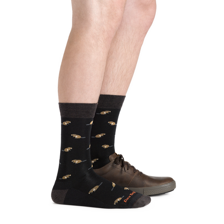 Side studio shot of model wearing men's sawtooth crew lifestyle sock in black with one brown shoe on left foot