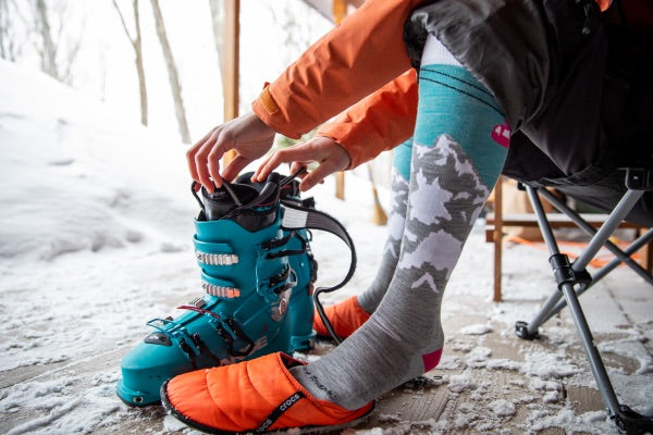 Skier with knee high ski socks on, about to put on their ski boots