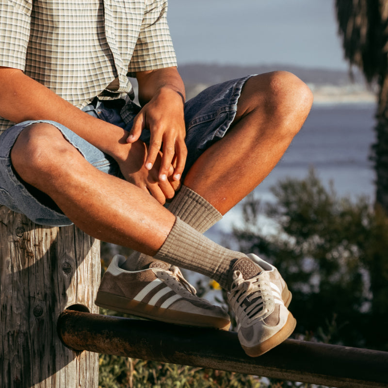 A man seated on a fence wearing tan Darn Tough socks with matching sneakers