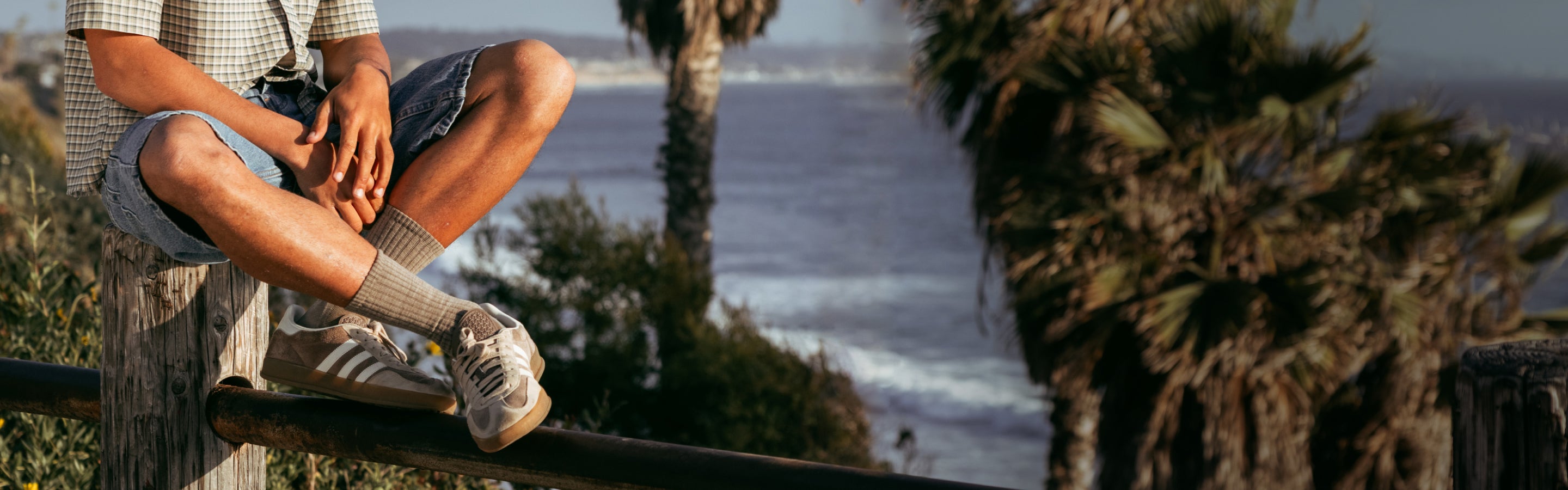 A man seated on a fence wearing tan Darn Tough socks with matching sneakers