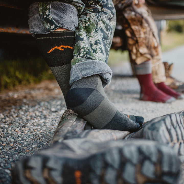 Lifestyle photo of 2101 heavyweight boot sock , man with feet crossed and women's feet blurred in background.
